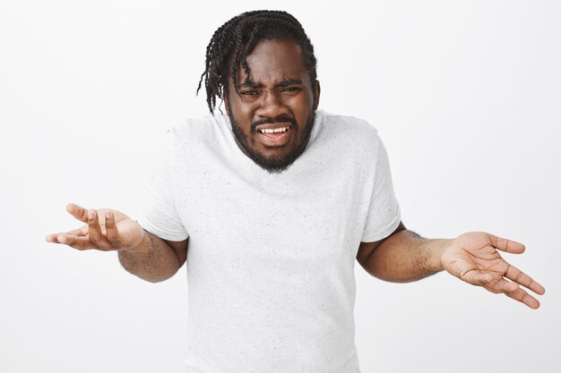 Portrait of frustrated guy with braids posing against the white wall