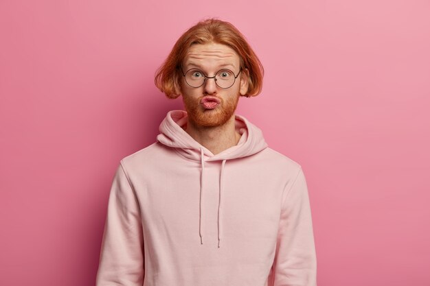 Portrait of funny bearded man with bob hairstyle, pouts lips and makes grimace