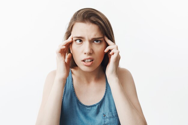 Portrait of funny beautiful young brunette woman with straight hair massaging head with finger, having super tired look after receiving lot of tasks on work.