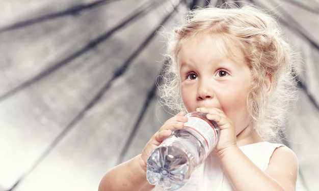 Portrait of a funny cute little girl in a casual dress, drink water while sitting in a studio.