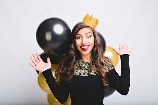 Портрет смешной взволнованной девушки празднует новый год с золотыми и черными шарами