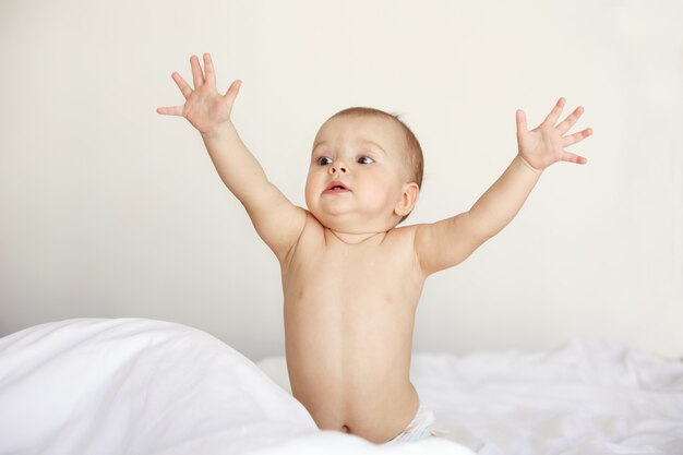 Portrait of funny nice baby woman stretching hands sitting in bed at home.