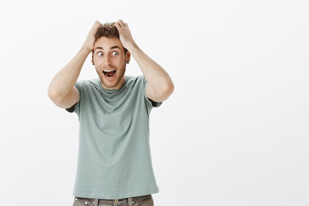 Portrait of funny weird european guy in trendy t-shirt, pulling out hair from head, looking left while screaming out loud, acting crazy and strange