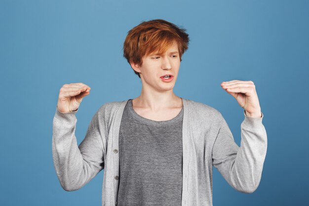 Free photo portrait of funny young attractive guy with ginger hair in casual clothes making faces with hands, talking to them with silly face, trying make his little sister to laugh.