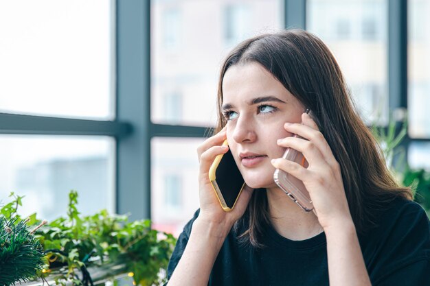 두 대의 전화기로 통화하는 재미있는 젊은 여성의 초상화