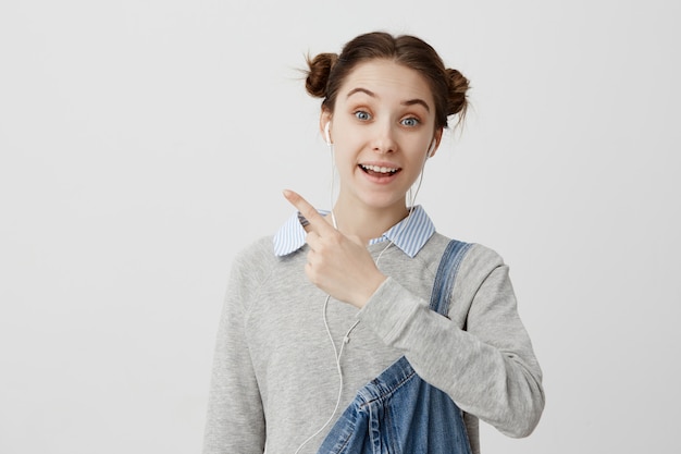 portrait of funny young woman wearing denim pointing index finger away. Happy facial expressions of female fashion designer relaxing before presentation with calm music. Copy space