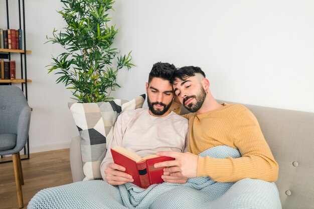 Portrait of gay couple relaxing together on sofa while reading the book