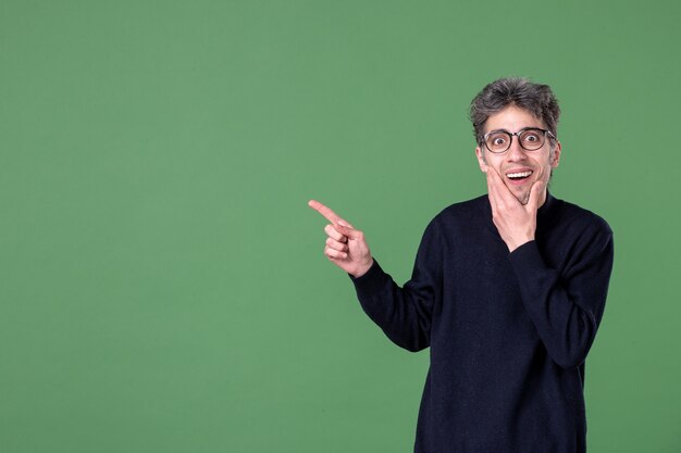 Portrait of genius man dressed casually in studio shot pointing aside green wall