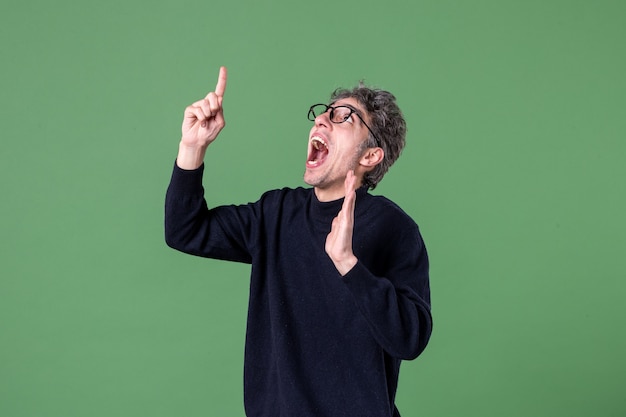 Portrait of genius man dressed casually in studio shot pointing above green wall