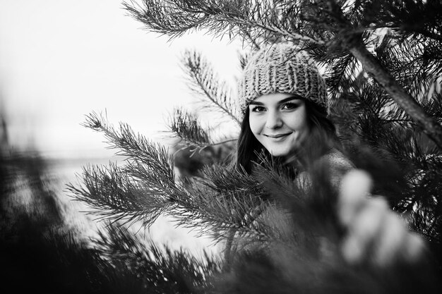 Портрет нежной девушки в сером пальто и шляпе на фоне новогодней елки на открытом воздухе