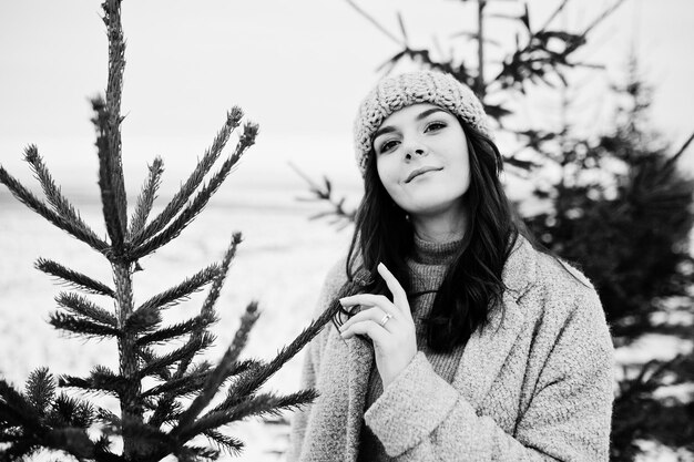 Portrait of gentle girl in gray coat and hat against new year tree outdoor