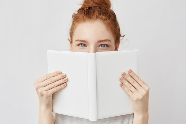 Portrait of ginger woman hiding behind book.