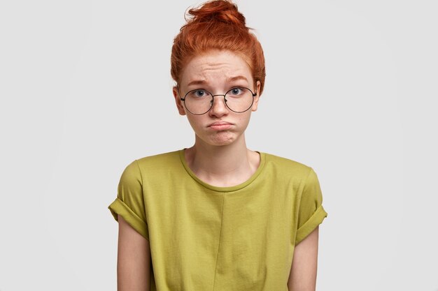 Portrait of ginger woman purses lower lip in discontent, feels insult as hears negative comments, wears casual bright t shirt