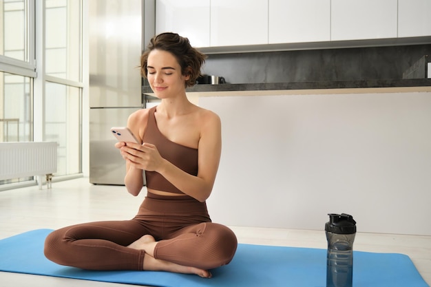 Foto gratuita ritratto di ragazza che fa yoga a casa utilizzando l'app per smartphone e sorridendo monitorando i progressi dell'allenamento al mo