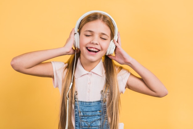 Free photo portrait of a girl enjoying the music on headphone standing against yellow background