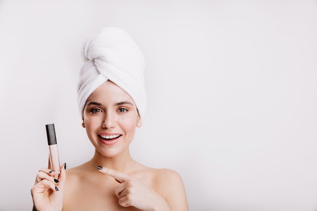 Portrait of girl in high spirits during morning routine on white wall. Model shows eye concealer.