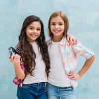 Free photo portrait of a girl holding camera in hand standing with her friend looking to camera