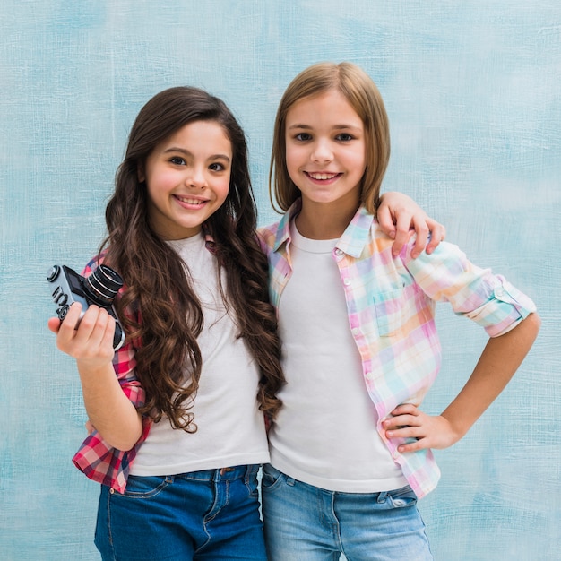 Portrait of a girl holding camera in hand standing with her friend looking to camera