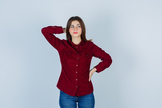 Портрет девушки в бордовой блузке, держащей руку за головой и задумчивой