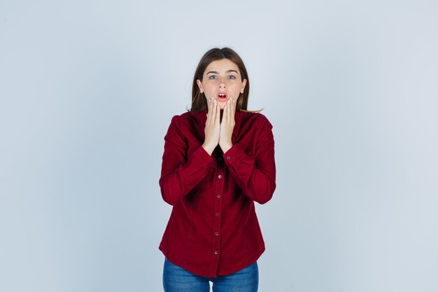 Portrait of girl holding hands on chin in casual shirt and looking surprised