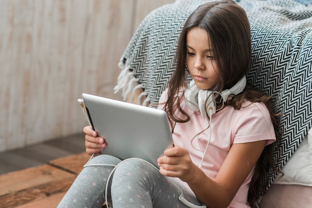 Foto gratuita ritratto di una ragazza guardando la tavoletta digitale con cuffia intorno al collo