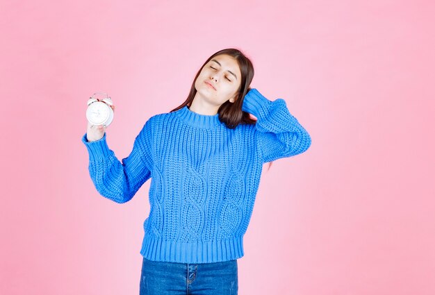 Portrait of a girl model holding an alarm clock on pink wall.