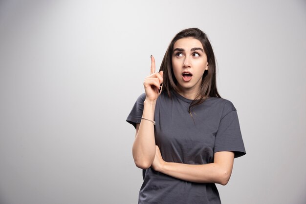 Portrait of a girl pointing up over a gray wall.