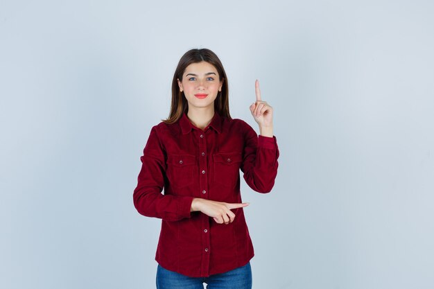 Portrait of girl pointing up and right in burgundy shirt and looking jolly