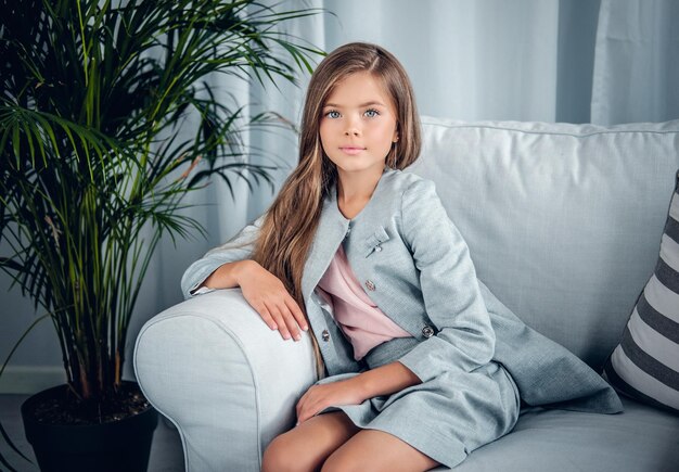 Portrait of a girl posing on a sofa in a living room with green plants.