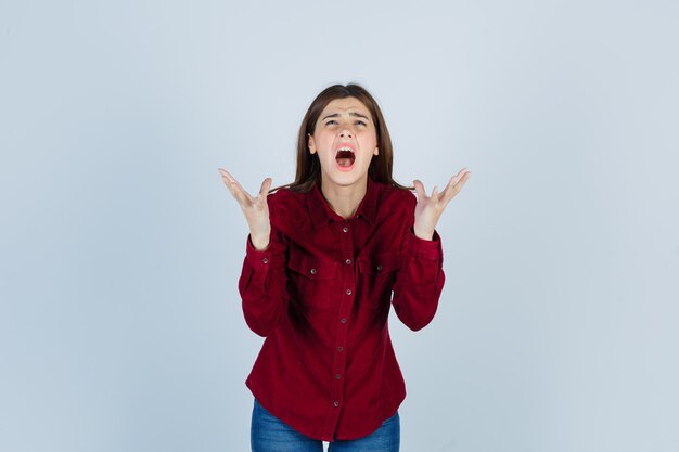 Portrait of girl raising hands while screaming in burgundy shirt and looking wistful