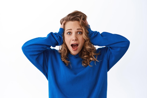 Portrait of girl in shock panicking holding hands on head and looking troubled and alarmed white background