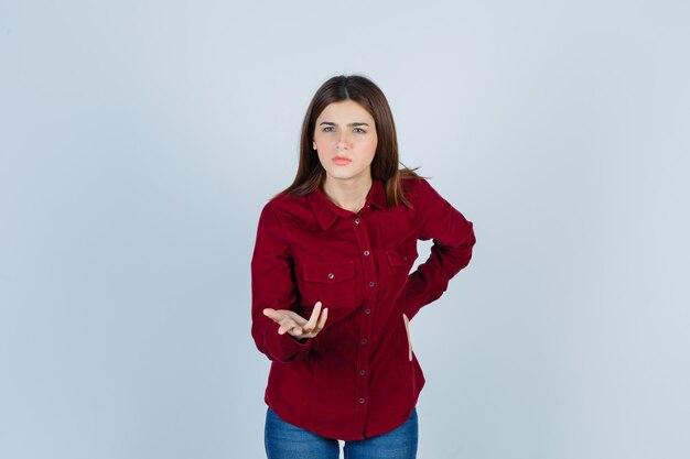 Portrait of girl showing asking question gesture in burgundy shirt and looking puzzled