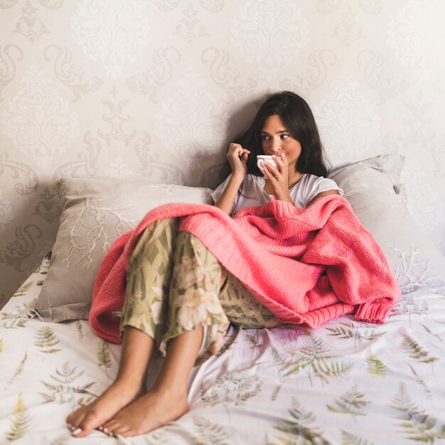 Portrait of a girl sitting on bed drinking coffee