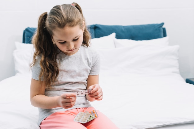 Portrait of a girl sitting on bed looking at blisters of pharmaceutical pills