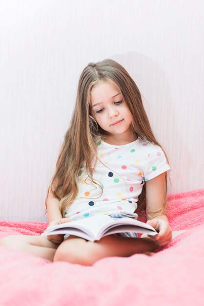 Portrait of a girl sitting in soft pink bed reading book