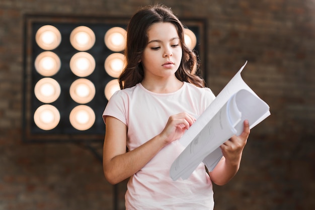 Portrait of girl standing against stage reading script