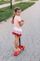 Free photo portrait of a girl standing on red push scooter looking at camera