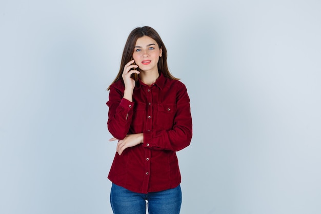 Free photo portrait of girl talking on smartphone in burgundy shirt and looking cheerful