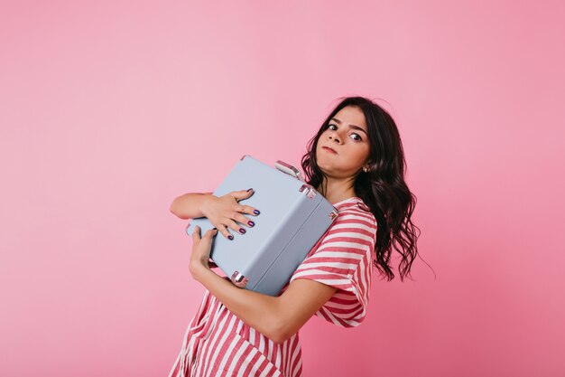 Portrait of girl tightly holding heavy briefcase. Brown-eyed lady leaned under weight of bag.