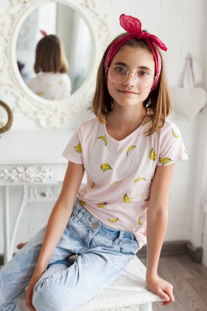 Portrait of girl wearing spectacle sitting on table looking at camera