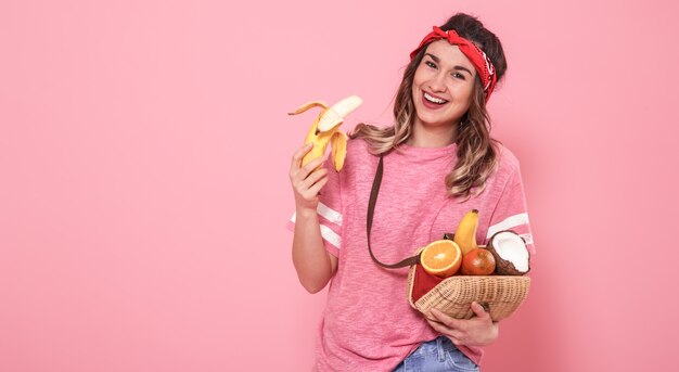 Portrait of a girl with healthy food, fruits, on a pink wall