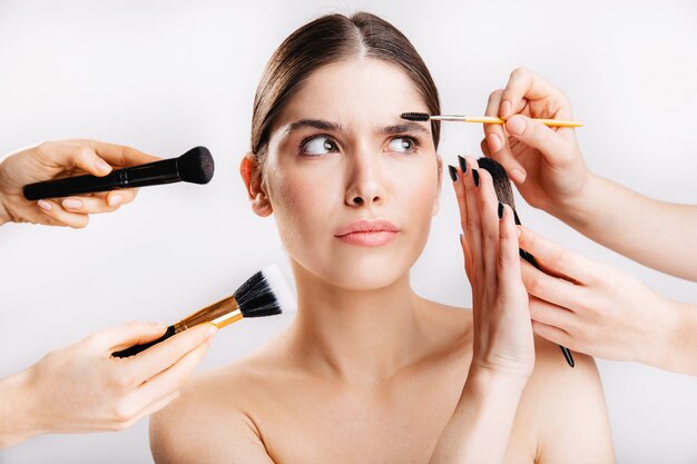 Portrait of girl with healthy skin on white wall. Woman doesn't want to do makeup and removes from her face brushes.