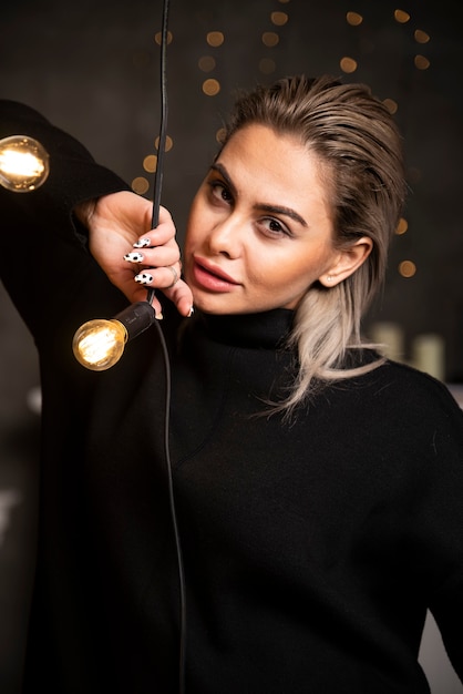 Free photo portrait of a glad pretty woman in dark sweater standing near lamps .