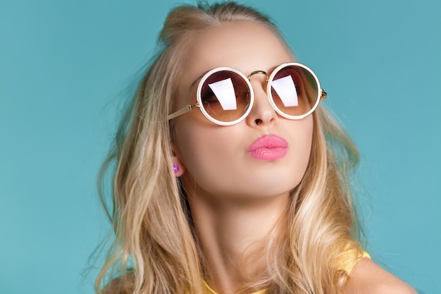 Portrait of glamorous beautiful blond woman in sunglasses and yellow shirt on blue background. carefree summer.