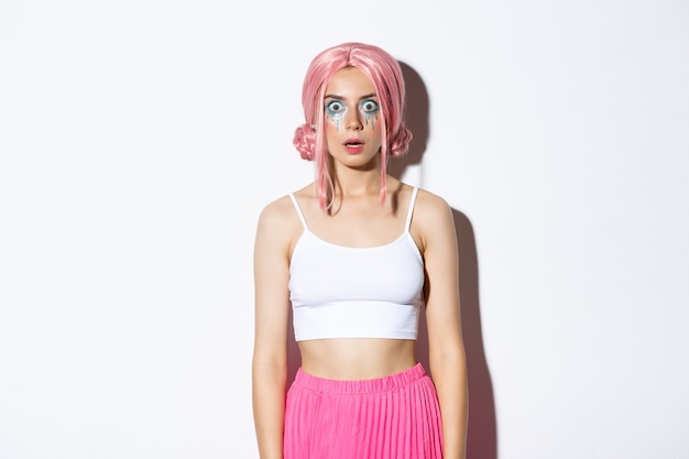 Free photo portrait of glamorous party girl in pink wig and bright makeup, drop jaw and looking startled at camera, stare at something impressive, standing.