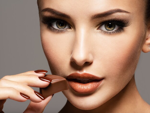 Portrait of glamour beautiful woman holds and eats  chocolate candy. Photo in brown color style