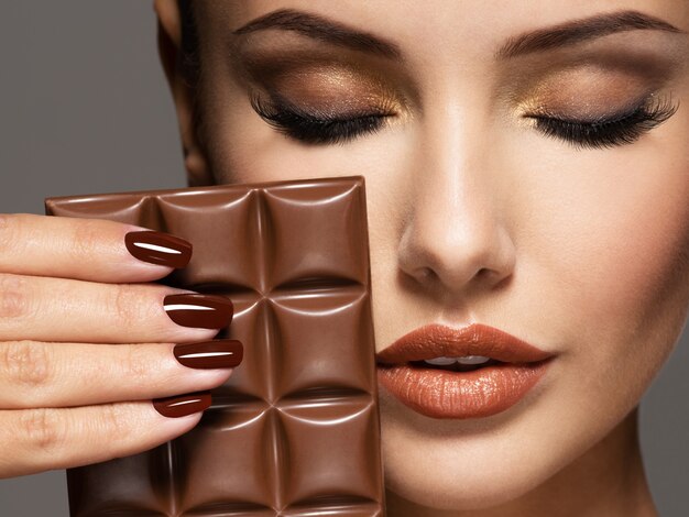 Портрет гламура Красивая женщина с коричневыми ногтями держит плитку шоколада