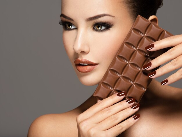 Portrait of glamour Beautiful woman with brown nails holds bar of chocolate