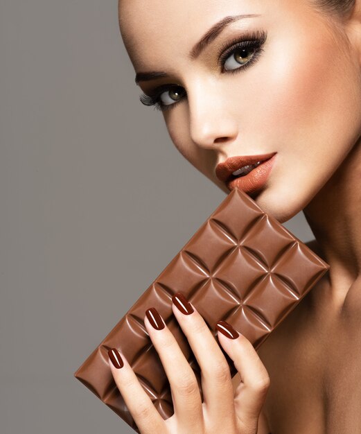 魅力の肖像画茶色の爪を持つ美しい女性はチョコレートのバーを保持します