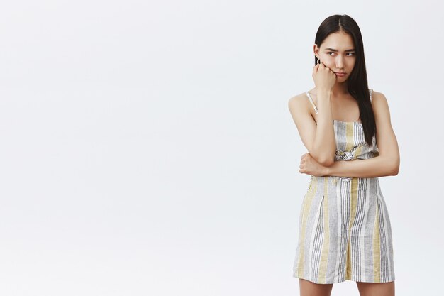 Portrait of gloomy and moody cute asian female in trendy outfit, leaning on fist and gazing down, upset